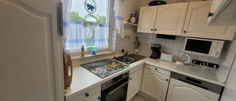 A kitchen with white cabinets, a stove, a microwave, and a window with a blue curtain.