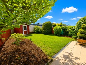A well-maintained garden with a lawn, a small shed, and a variety of shrubs. - Vacation home SÜDWIND for 4 people near the beach and North Sea in Butjadingen-Tossens (Butjadingen-Tossens)