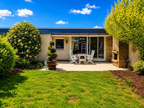 A house with a patio, a small table with chairs, a potted plant, and a brick fireplace. - Vacation home SÜDWIND for 4 people near the beach and North Sea in Butjadingen-Tossens (Butjadingen-Tossens)
