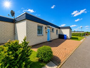 A single-story building with a brick facade, a blue door, and a satellite dish. - Vacation home SÜDWIND for 4 people near the beach and North Sea in Butjadingen-Tossens (Butjadingen-Tossens)