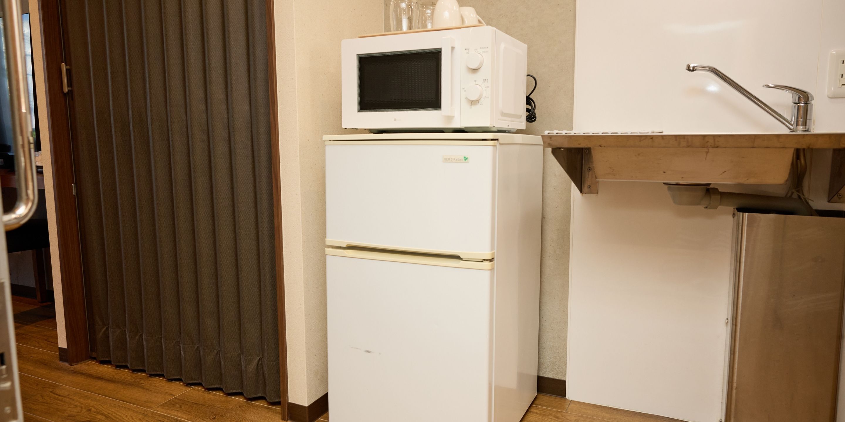 Pieni, käytännöllinen keittiönurkkaus, jossa on valkoinen jääkaappi, mikroaaltouuni ja pesuallas.