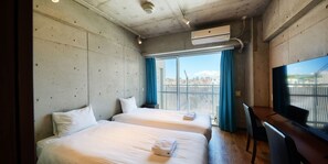 A hotel room with two beds, a desk, a TV, and a large window with a city view. - New Normal Hotel in NAHA WAKASA (Naha)