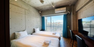 Habitación de hotel con dos camas, un escritorio, televisor y un ventanal con vista a la ciudad.