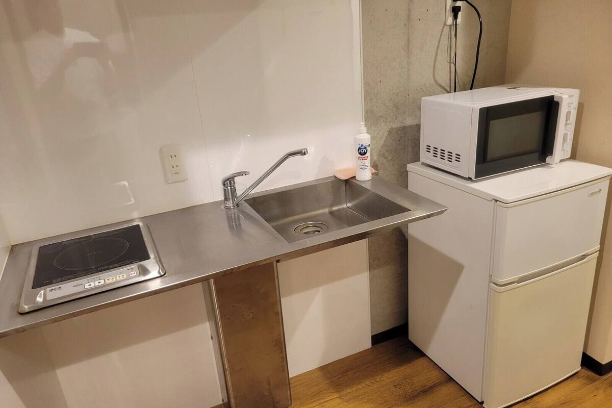 Cozinha compacta com fogão embutido, pia, micro-ondas e geladeira pequena.
