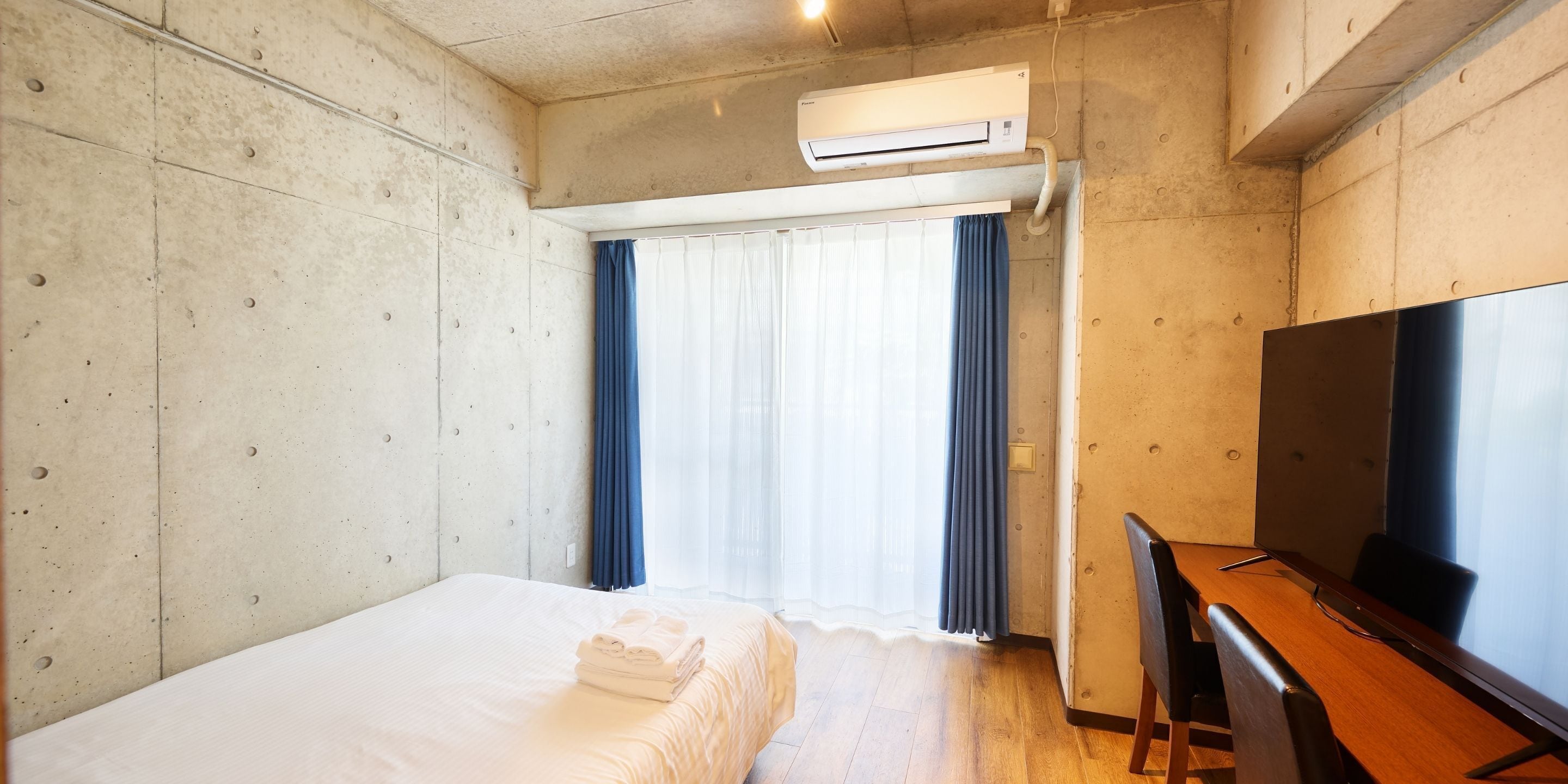 Hotellihuone, jossa on sänky, työpöytä, televisio ja ilmastointilaite.