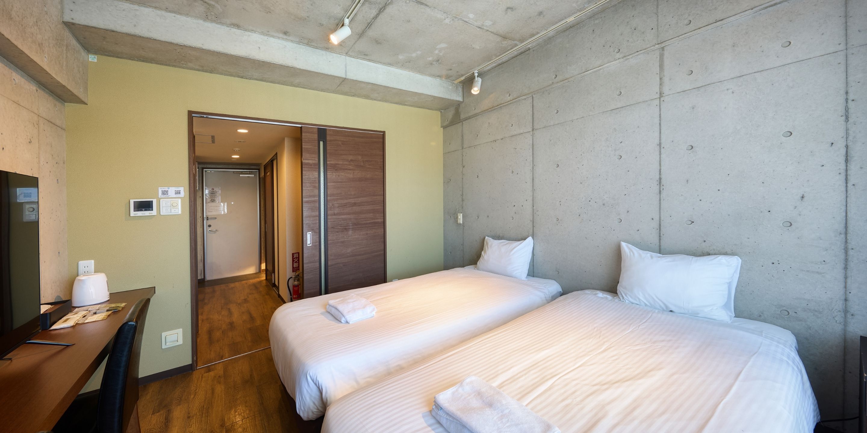 A hotel room with two beds, a desk, and a wardrobe.
