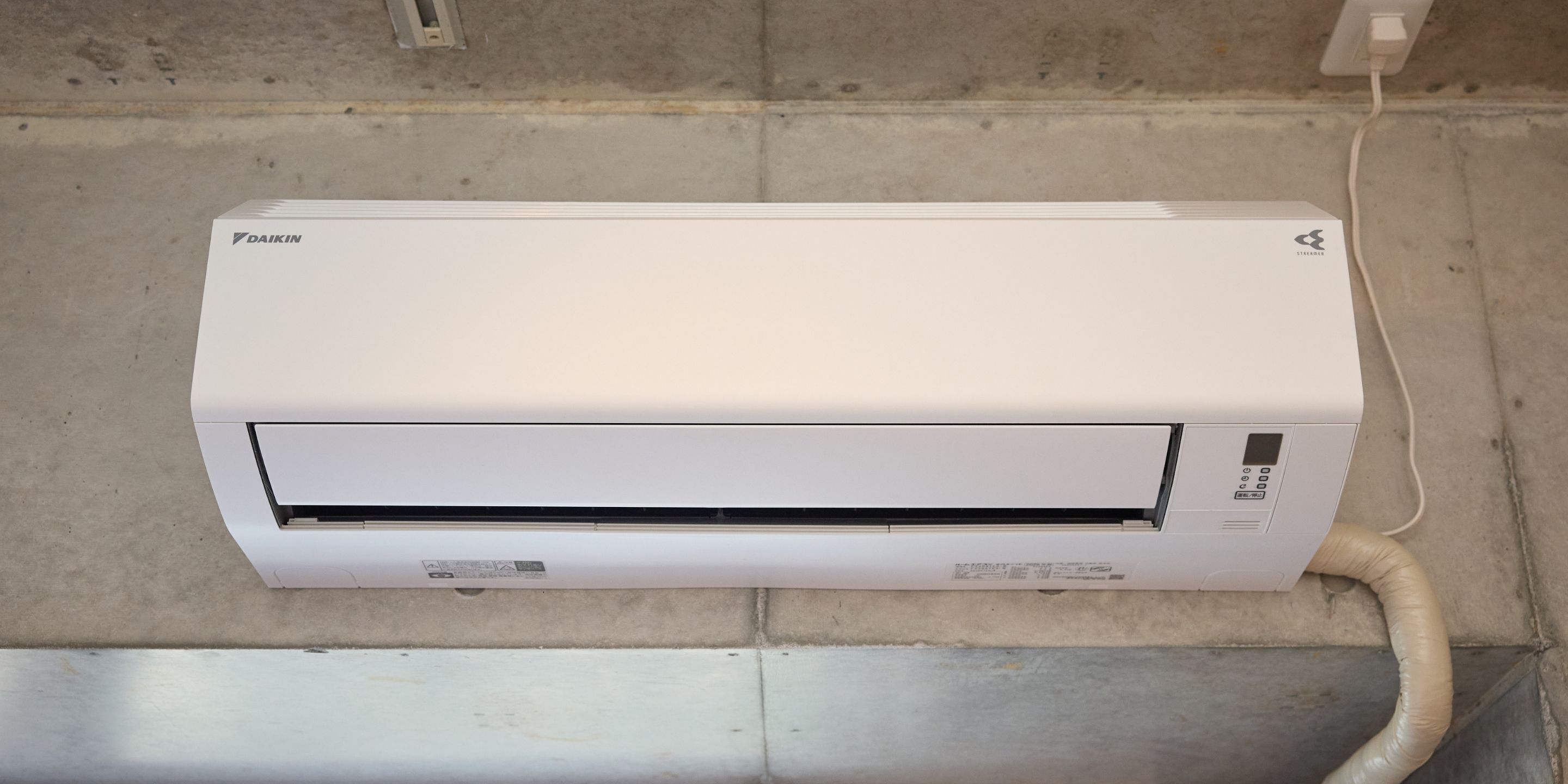 A Daikin air conditioner unit mounted on a wall with a visible power cord.