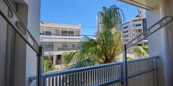 A balcony with a metal railing, overlooking a residential area with multi-story buildings and a palm tree.