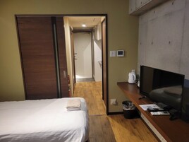 Una habitación de hotel con una cama, televisor, escritorio con computadora y un basurero.
