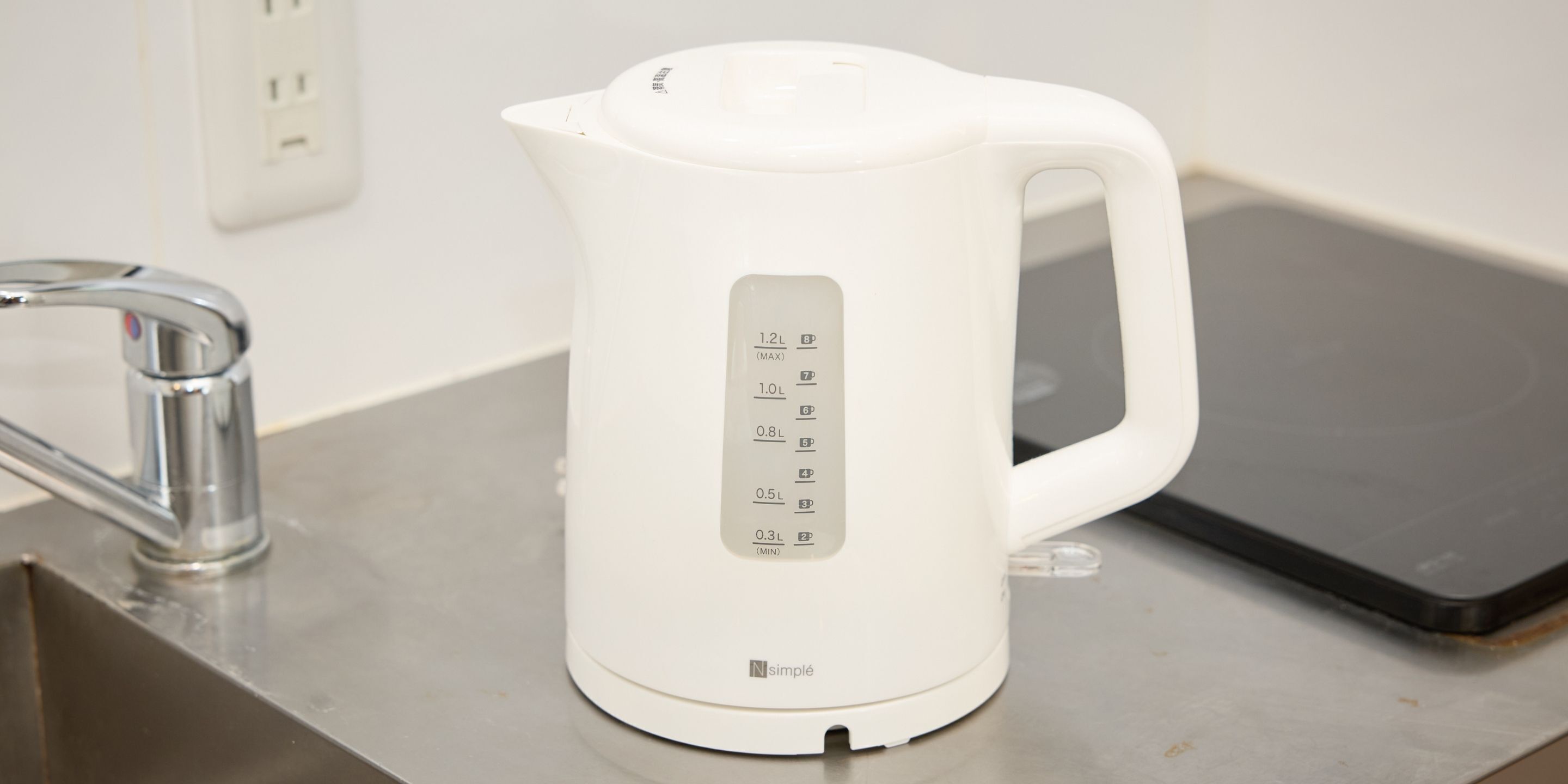 A white electric kettle with measurement markings on a kitchen counter.