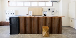 A reception desk with a wooden finish, a black storage unit, and a small wooden stool. - New Normal Hotel in NAHA WAKASA (Naha)