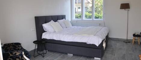 A bedroom with a bed, a chair, a lamp, and a window.