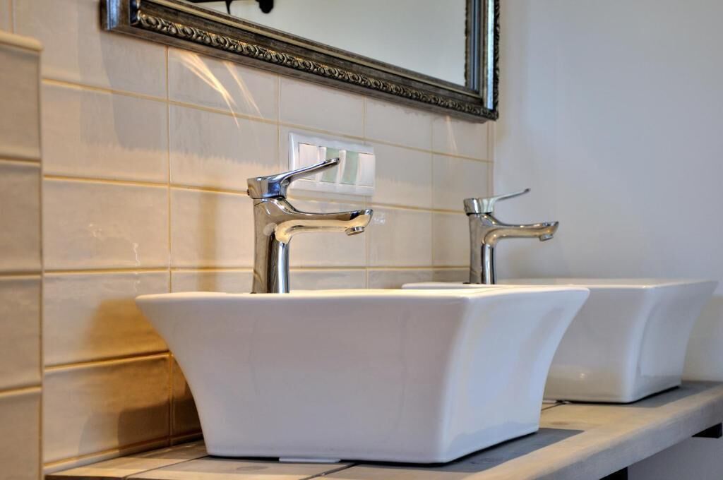 A bathroom with two white sinks, a mirror with an ornate frame, and a light switch on the wall.
