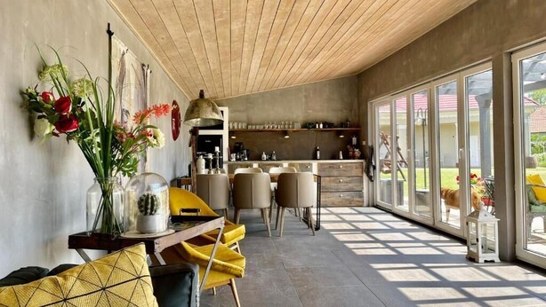 A modern kitchen with a dining area, large windows, and a dog visible outside.