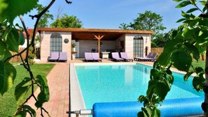 A pool area with lounge chairs, a covered seating area, and a clear blue pool.
