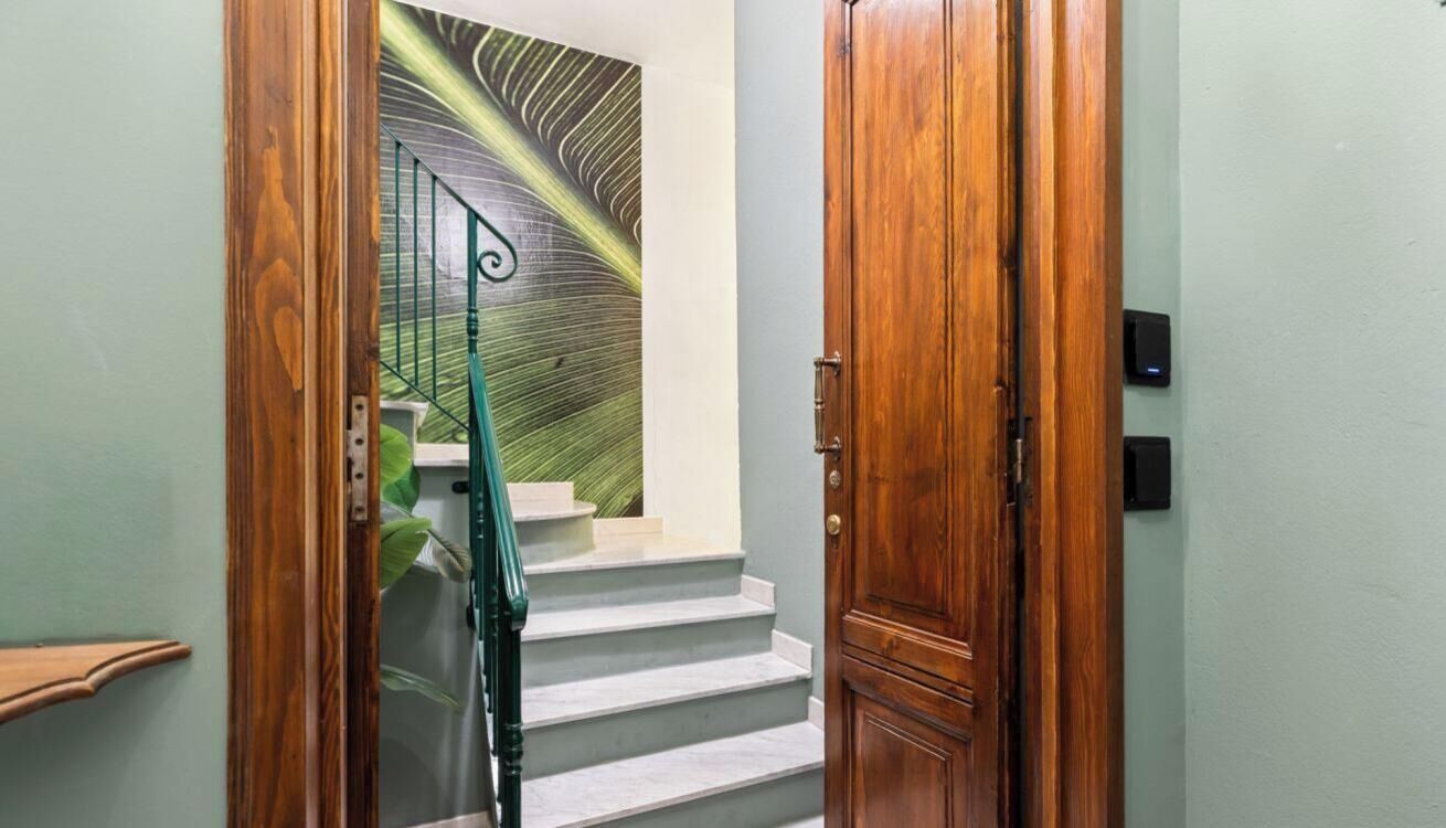 Eine Holztür, eine Treppe mit grüner Geländer und eine Wand mit einem Blattmuster.