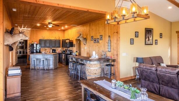 A rustic interior with a wooden ceiling, a bar area, a dining table, and a sofa.