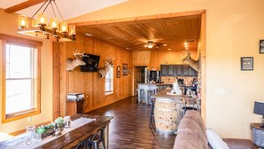 A spacious living area with a wooden ceiling, a dining table, and a bar area with a mounted deer head.