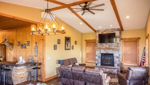 A rustic interior with a stone fireplace, leather sofas, a wooden bar, and a ceiling fan.
