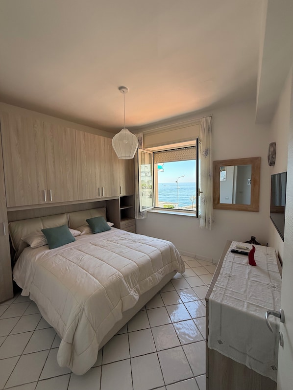 A bedroom with a bed, a bedside table, a mirror, and a window with a view of the sea. - Masticiello House (Nerano)