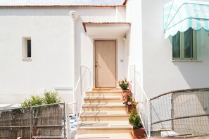 A white building with a wooden door, a small window, and a balcony with a striped awning. - Masticiello House (Nerano)