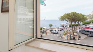 Vista dalla finestra su una strada con auto parcheggiate, un attraversamento pedonale e uno specchio d'acqua all'orizzonte.