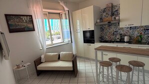 Una cucina moderna con mobili bianchi, un'area pranzo con sgabelli, un divano e una finestra con tende.