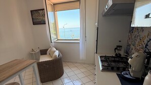 Una cucina compatta con piano cottura a gas, macchina da caffè e vista mare attraverso una finestra.
