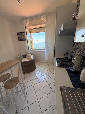 A compact kitchen with a gas stove, a coffee maker, and a view of the sea through a window. - Masticiello House (Nerano)