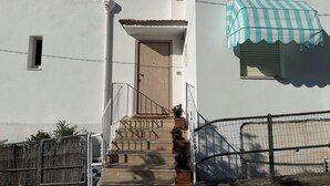 Un edificio bianco con una porta in legno, una piccola finestra e un tendaggio a righe.
