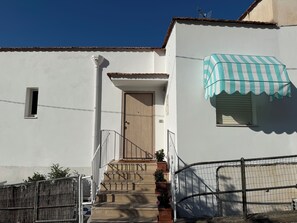 A white building with a wooden door, a small window, and a striped awning. - Masticiello House (Nerano)