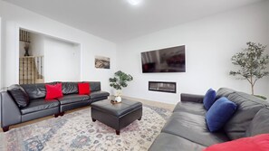 A modern living room with a black leather sofa, a grey sofa, a patterned rug, a small table with a vase, and a wall-mounted TV. - Private 5-bedroom Caledon Home Comfort, Style, and Nature! (Caledon)