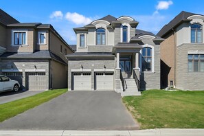 A residential neighborhood with houses featuring stone facades, multiple garage doors, and a well-maintained lawn. - Private 5-bedroom Caledon Home Comfort, Style, and Nature! (Caledon)
