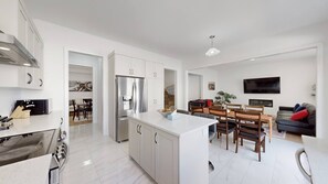 A modern kitchen with a central island, stainless steel appliances, and a dining area with wooden chairs and a table. - Private 5-bedroom Caledon Home Comfort, Style, and Nature! (Caledon)