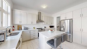 Uma cozinha moderna com armários brancos, eletrodomésticos de aço inoxidável e uma ilha central com assentos.