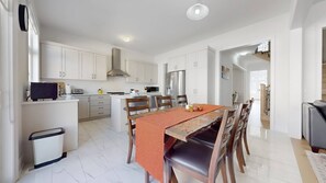 A modern kitchen with white cabinets, a dining area with a table and chairs, and a visible staircase leading to another level. - Private 5-bedroom Caledon Home Comfort, Style, and Nature! (Caledon)