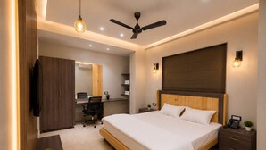 A modern bedroom with a large bed, a desk, a chair, a wardrobe, and a ceiling fan. - Studio 24 (Jaipur)