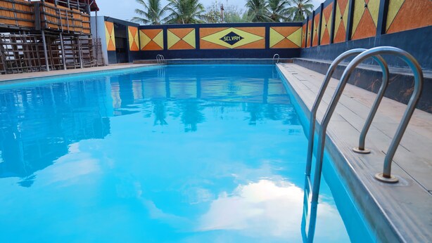 Une piscine avec un escalier en métal, entourée d’un mur coloré orné de motifs géométriques, sur lequel on peut lire le nom « SELVAM ».