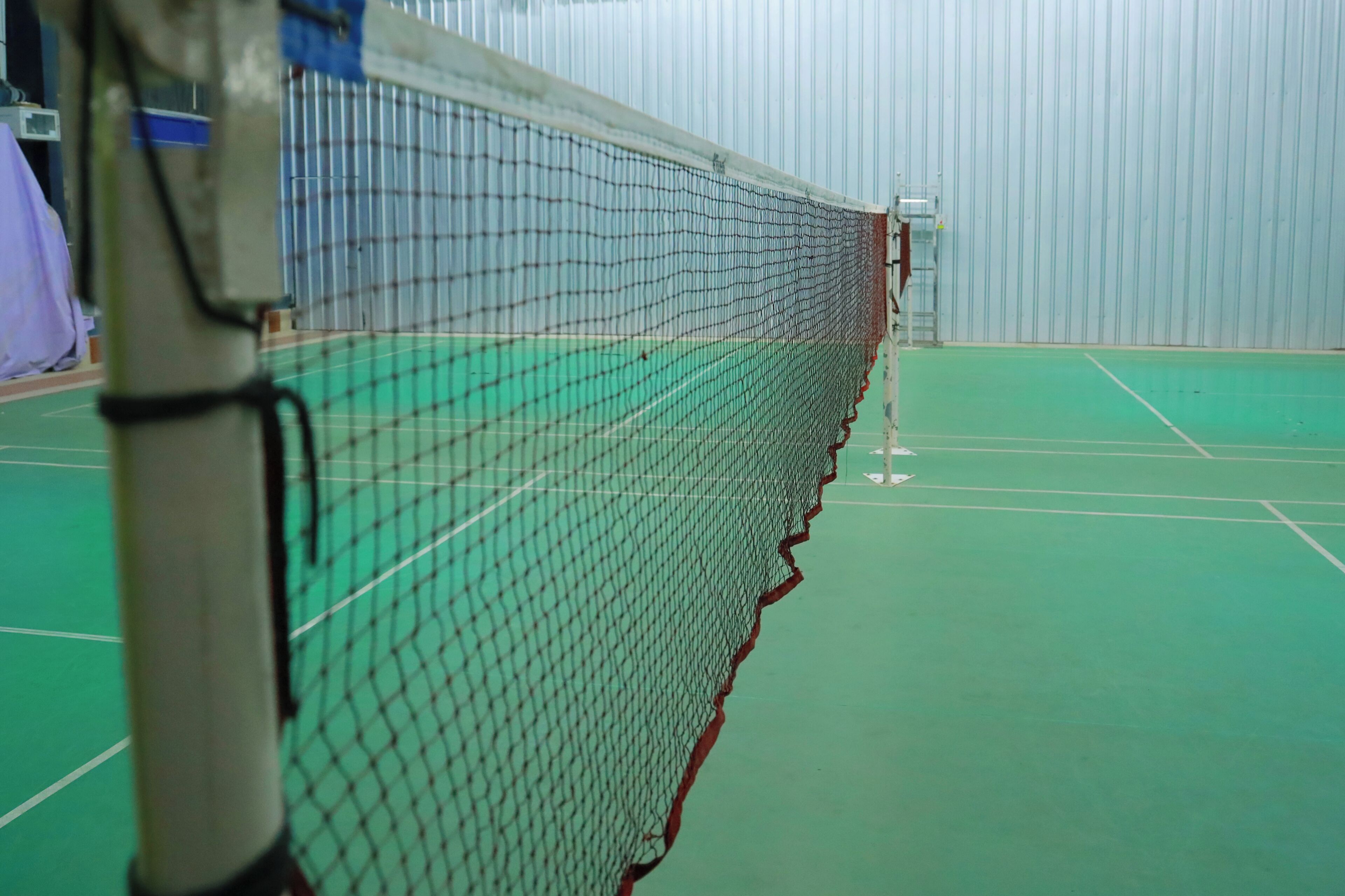 A tennis court with a net, green flooring, and a metal fence.