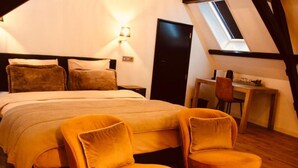 Un dormitorio con una cama, dos sillas, un escritorio y un tragaluz.