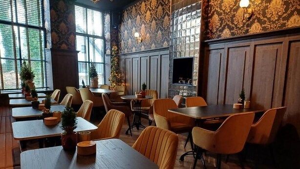 Un restaurante con mesas y sillas de madera, ventanas amplias y diseños decorativos en las paredes.