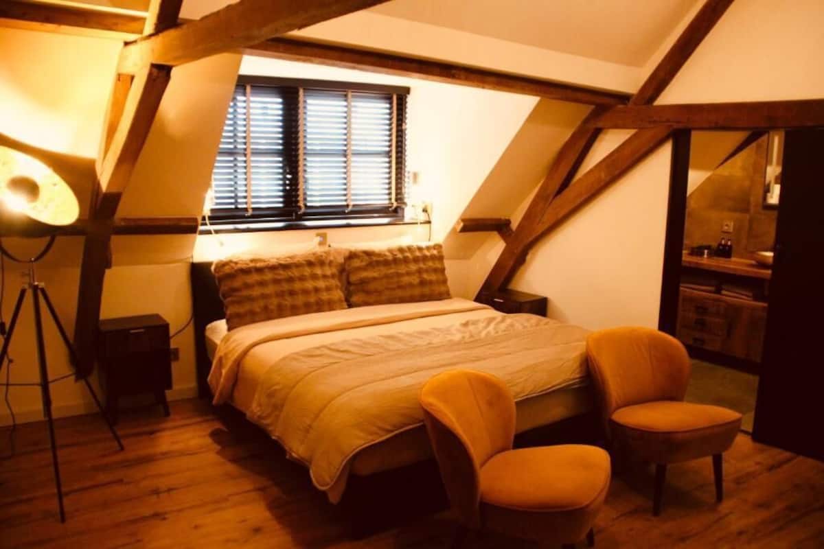 Un dormitorio con cama, dos sillas, escritorio y ventana con persianas.