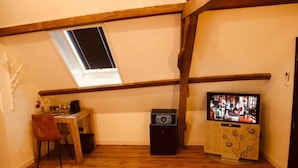 Una habitación con techo inclinado, un ventanal pequeño, un televisor, un escritorio con una silla y un altavoz.