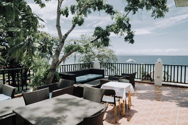 Une terrasse extérieure avec des meubles en osier, une table recouverte d’une nappe blanche et une vue sur la mer.