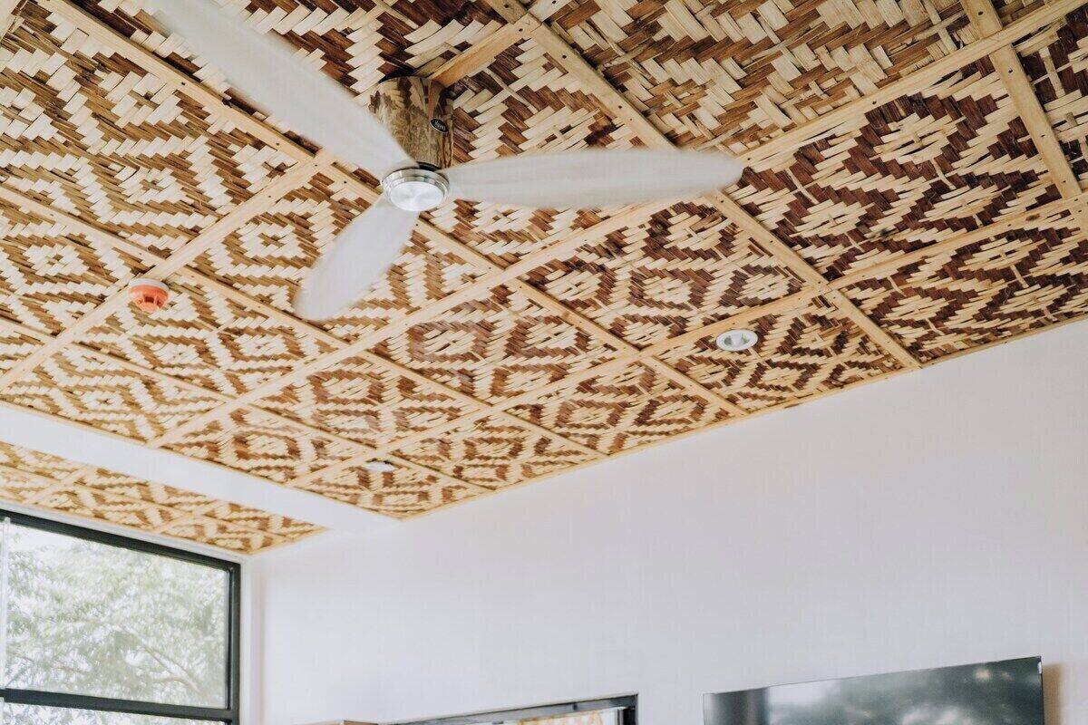 A bedroom with a bed, a wooden dresser, a TV, and a patterned ceiling.
