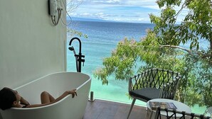 Una vasca da bagno con vista sull'oceano, un tavolo e sedie su un balcone.