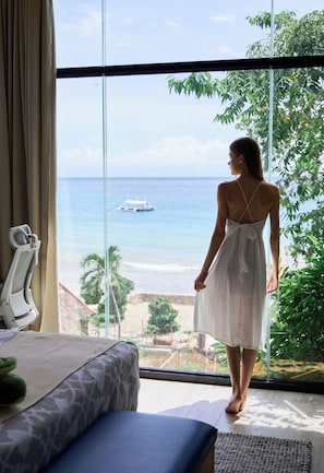 A room with a large window, a bed, a chair, and a view of the ocean.