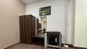 Habitació amb armari, taula petita, televisió penjada a la paret i un quadre amb marc.