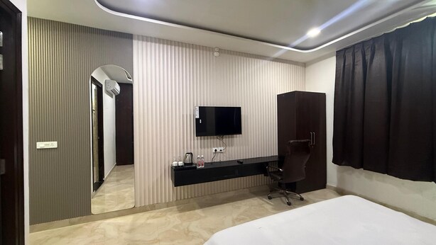 Habitació d'hotel moderna amb un llit gran, televisió de pantalla plana penjada a la paret, armari de fusta fosca i bany visible a través d'una porta.