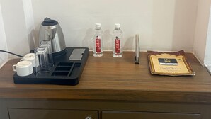 Escriptori d'habitació d'hotel amb una cafetera, dues ampolles d'aigua, un safata amb gots i un certificat emmarcat.